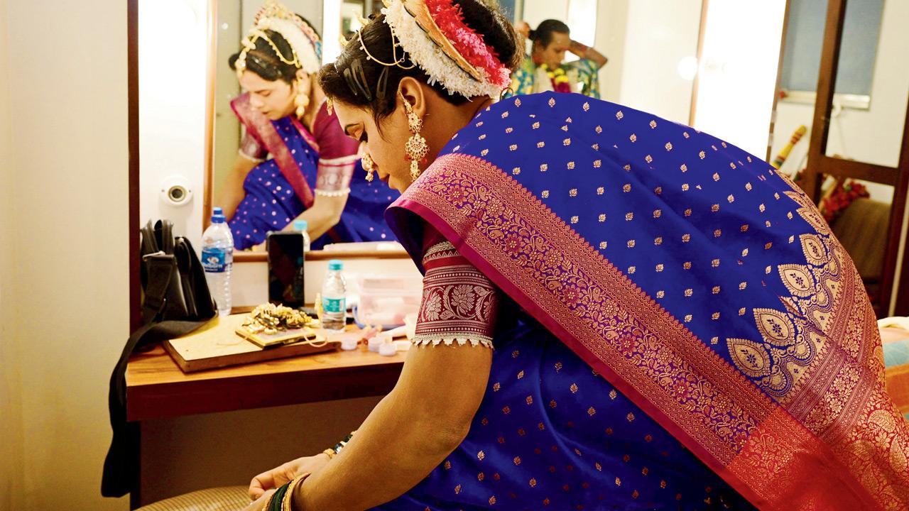 A male artiste portraying a female character carefully adjusts anklets, highlighting the intricate detailing involved in cross-gender roles