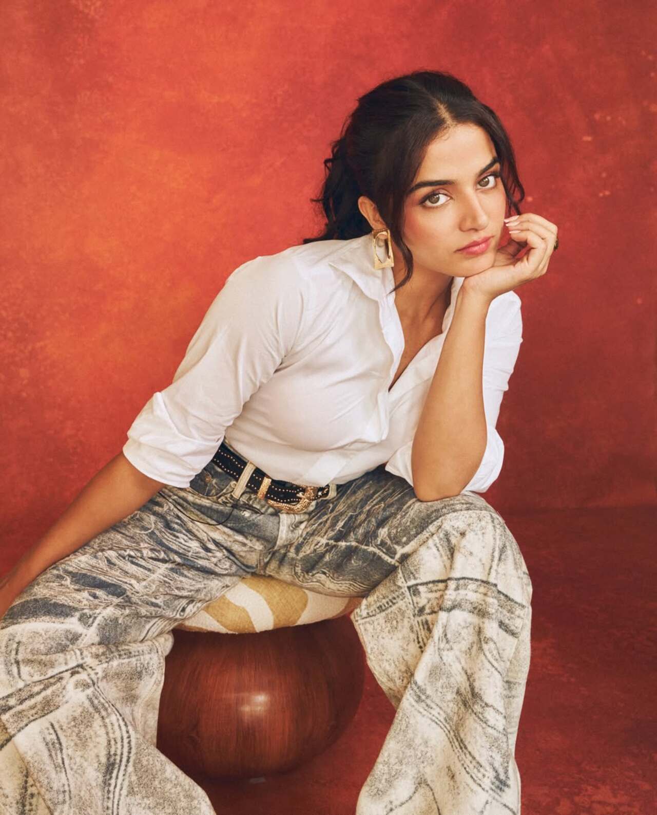 She adds a touch of edge with a chunky black belt and gold statement earrings, finishing the outfit with sleek white pointed-toe heels.