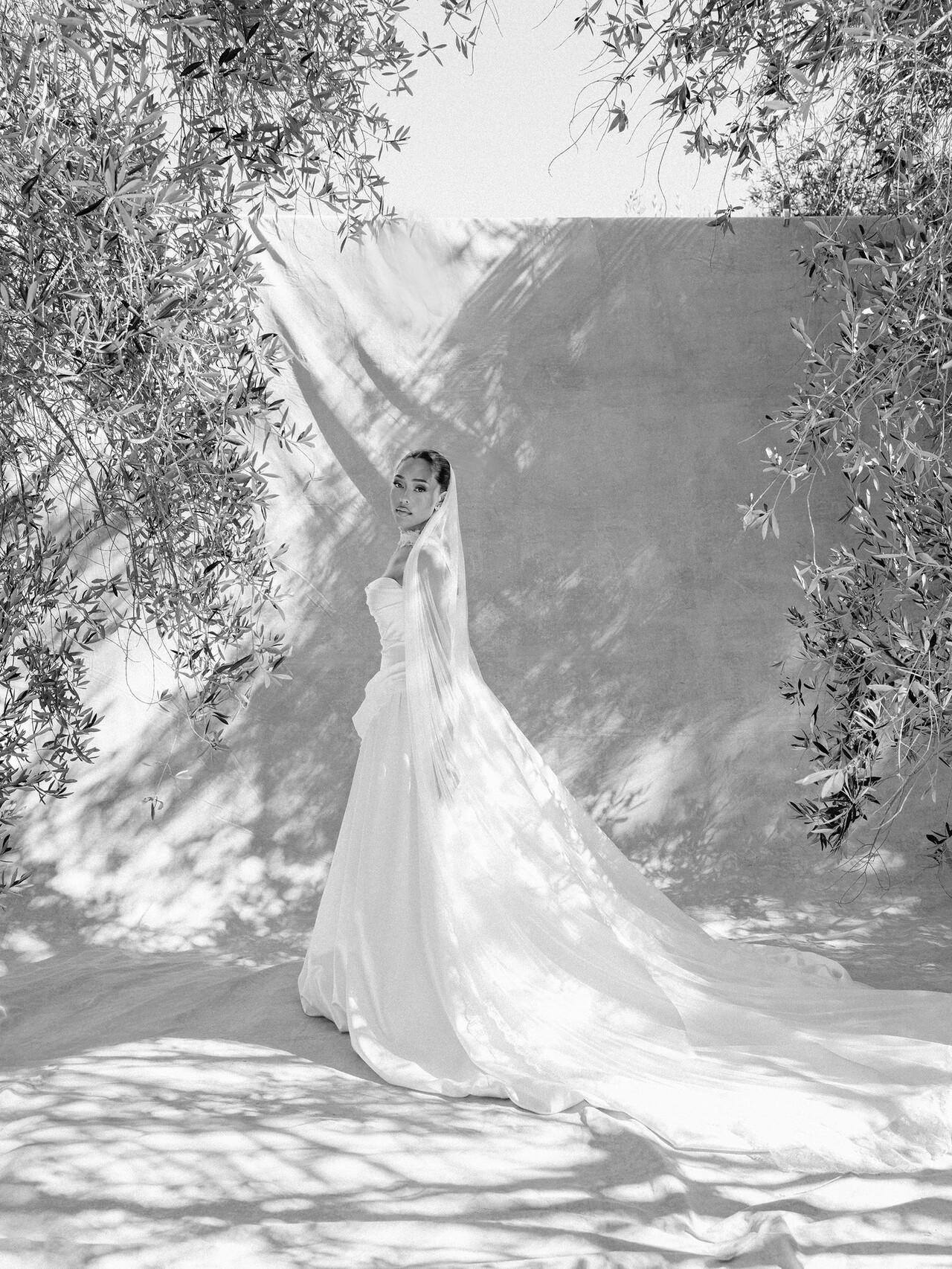 Jordyn Woods wears a custom Danielle Frankel wedding gown to celebrate her big day. The custom ballgown is constructed of strapless silk wool and features a draped bodice and full ball skirt.