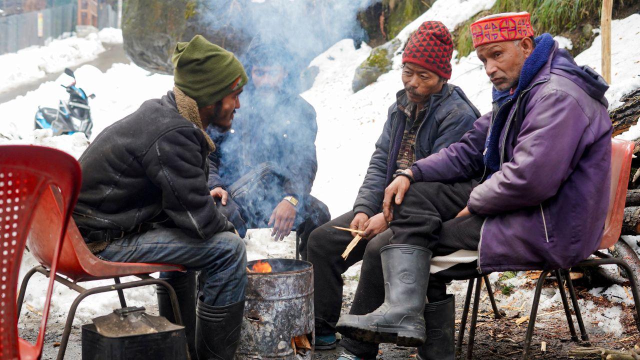 People warm themselves around a makeshift fire on a cold afternoon following fresh snowfall in Manali