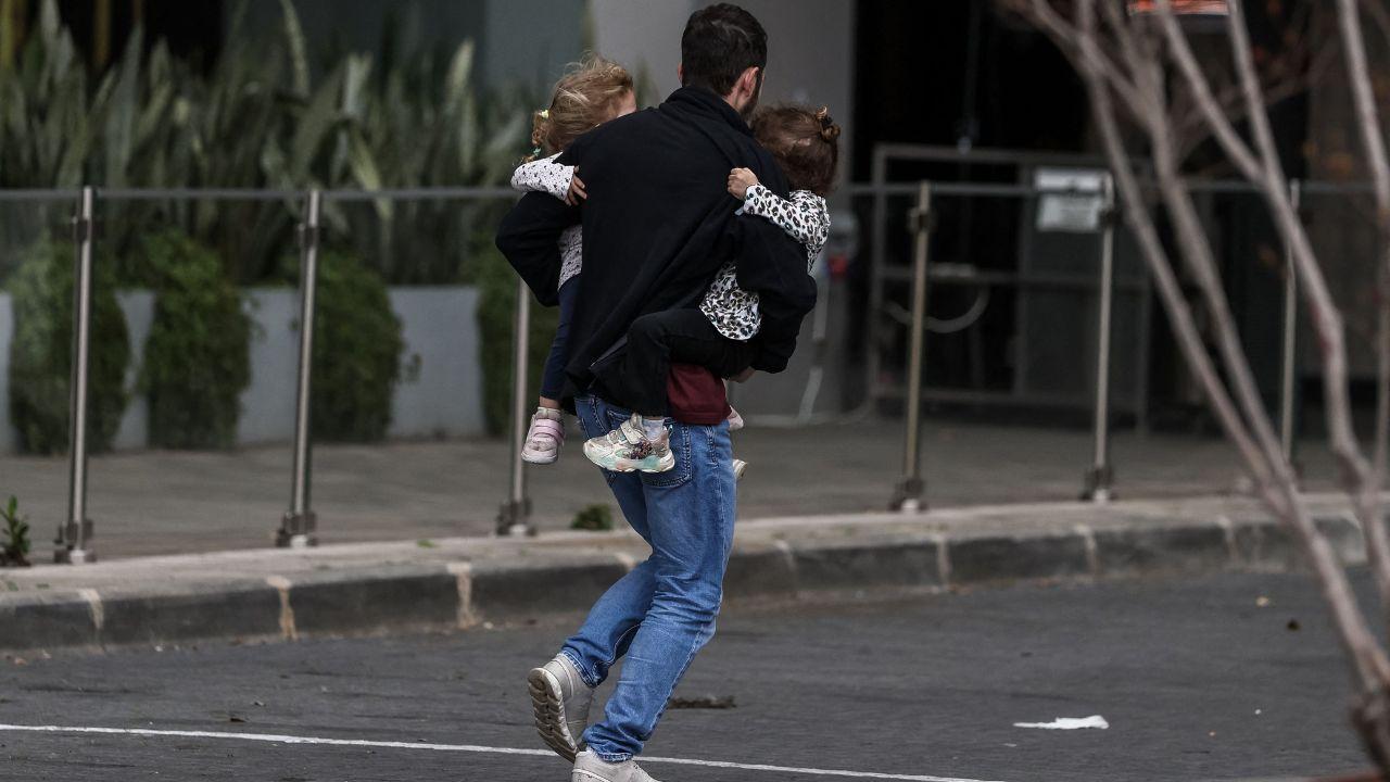 Air raid sirens sound in Jerusalem as authorities warn of incoming missiles following Israel’s preemptive strike. A man carries two children to safety in Tel Aviv as sirens echo nationwide, with civilians urged to remain close to bomb shelters
