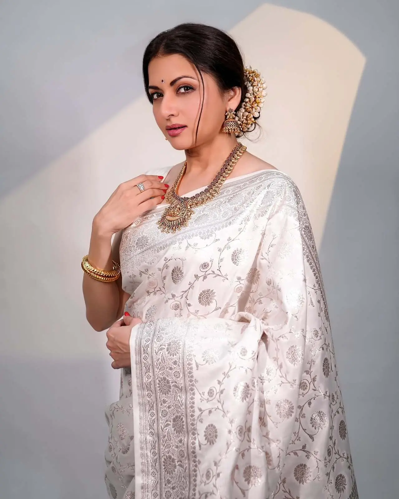 Bhagyashree looks effortlessly elegant in a white saree featuring delicate silver woven jaal detailing that adds a subtle shimmer. The classic drape is paired with traditional gold jewellery, enhancing the timeless charm.