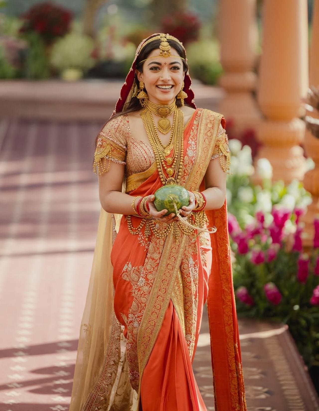 Rashmika was draped in a rich rust saree framed with a striking red border and a heavy blouse doused in golden accents. The saree featured a rich red-and-gold border and was teamed with a beige veil. She elevated her bridal look with an elaborate assemblage of traditional gold jewellery, including ornate necklaces, baajubandhs, a mathapatti, kadas and oversized jhumkas.