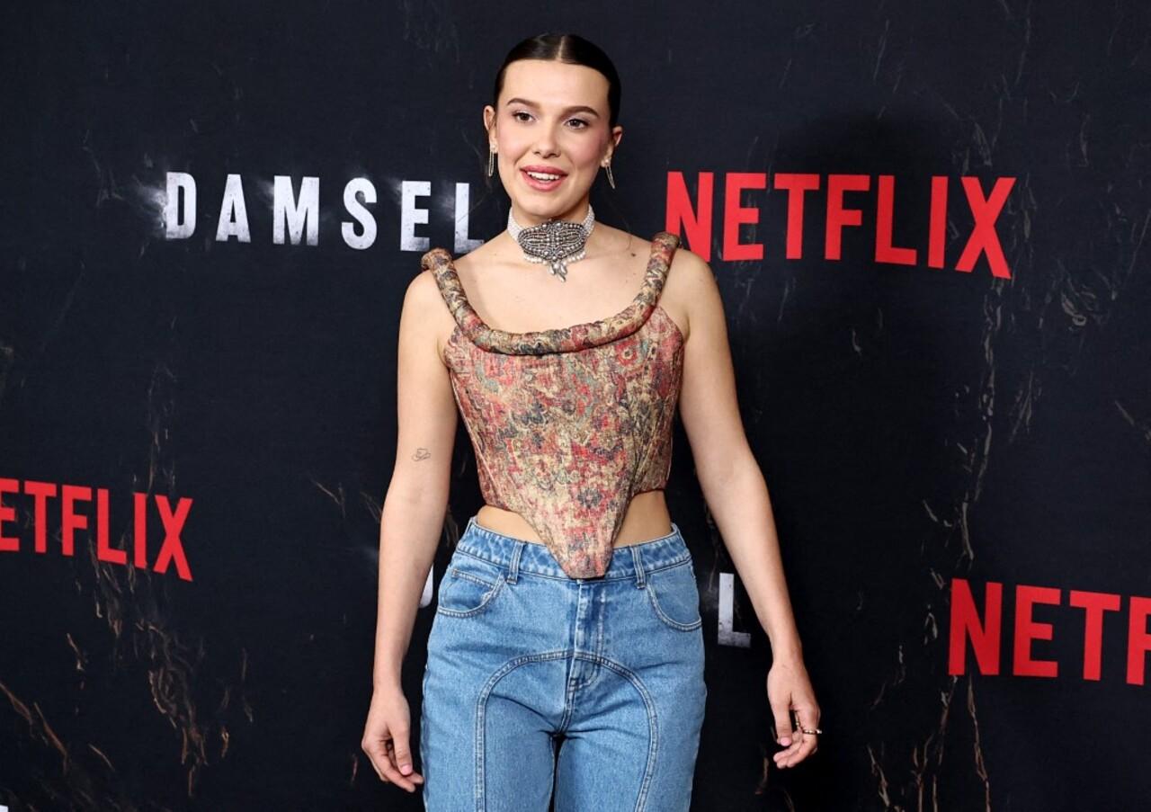 At the photo call for Damsel, Millie Bobby Brown mixed vintage and modern styles effortlessly. She wore a vintage-patterned corset top with light blue jeans, keeping it casual yet chic. A bold statement necklace added flair.