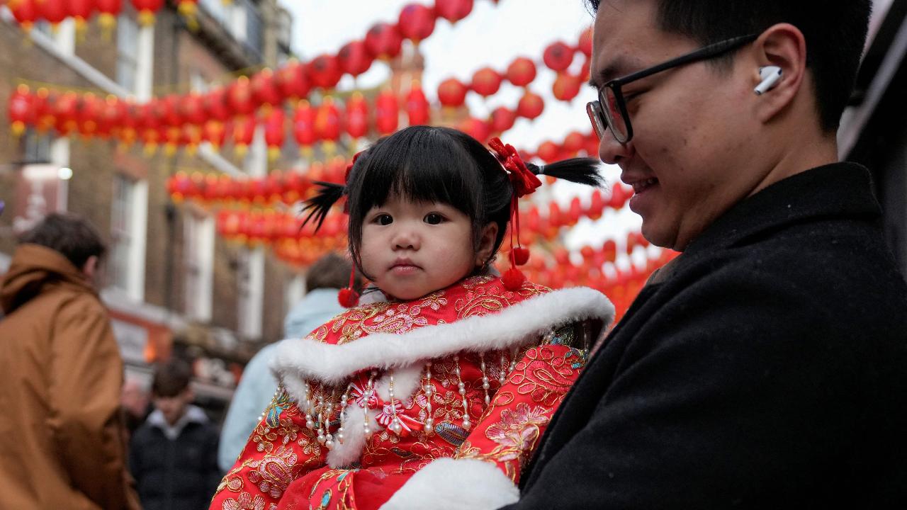 A man holds a toddler in traditional dress to mark the Year of the Horse along a street in Chinatown as people celebrate the first day of the Lunar New Year in London