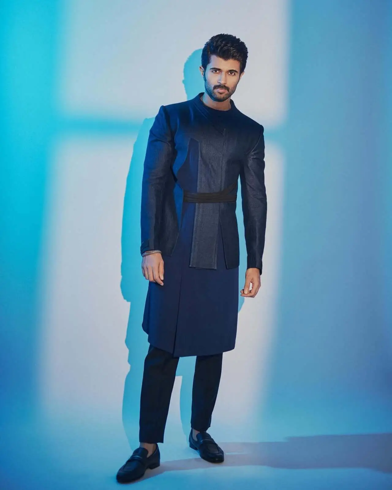 This is the ultimate Indo-Western fusion. The deep navy blue jacket features sharp, asymmetric paneling and a contrasting black belt, giving it a modern, almost military-inspired structure.