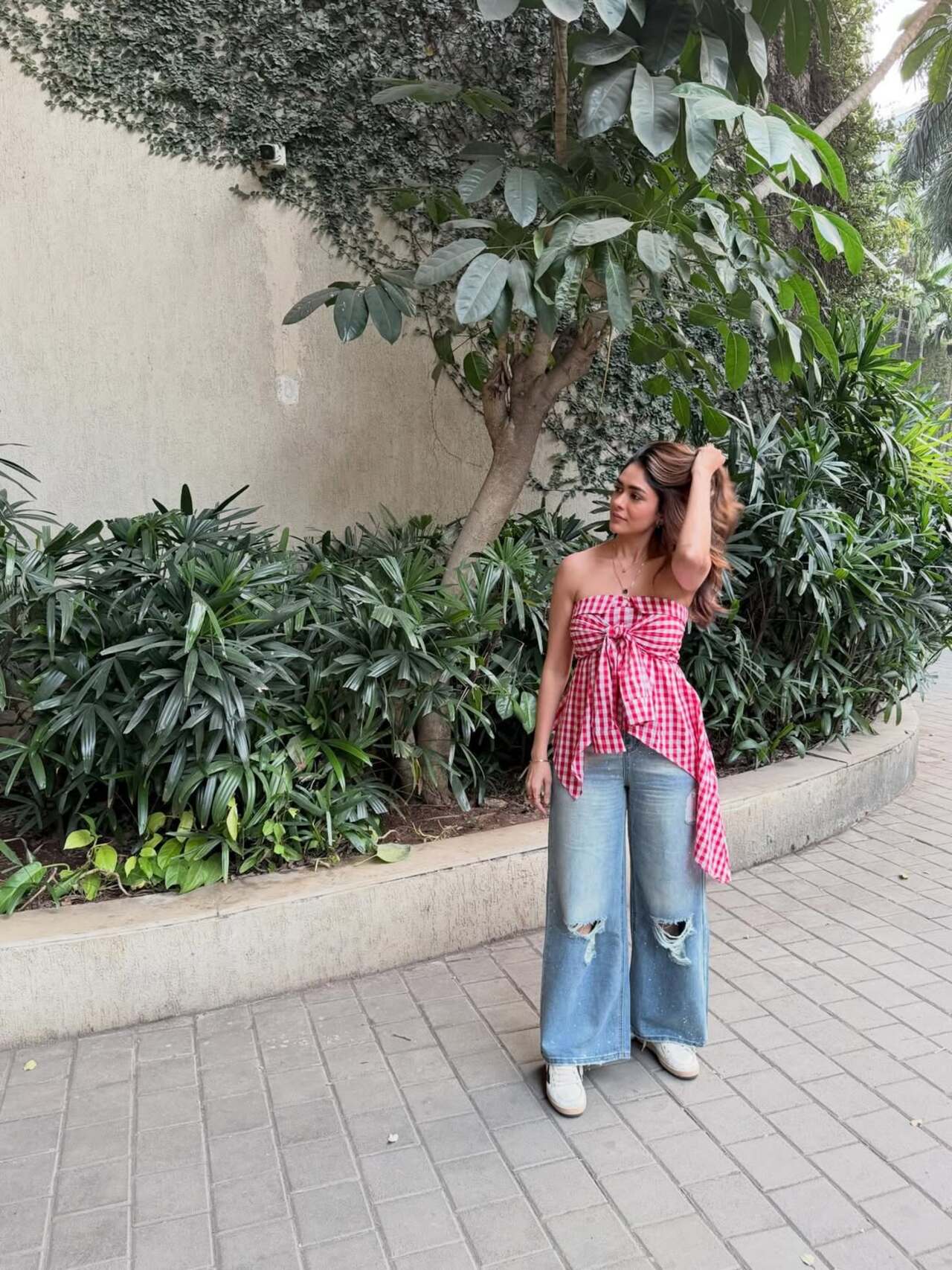 Mrunal keeps it stylish and casual in a red gingham strapless top with a bow detail in the front. The top is paired with wide-leg ripped denim jeans and white sneakers for a cool, relaxed vibe.