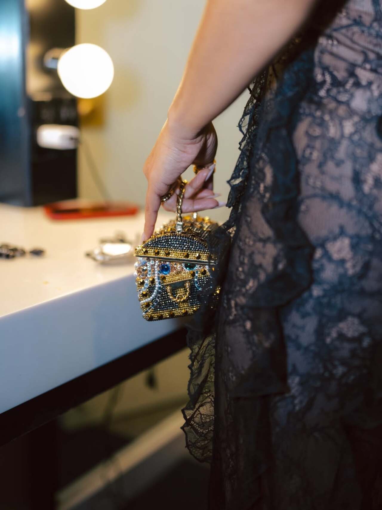 Priyanka elevated her sheer black lace dress with a striking statement minaudiere that instantly caught the eye. The miniature box clutch featured intricate gold detailing, studded embellishments, giving it a regal, almost vintage treasure-chest vibe.