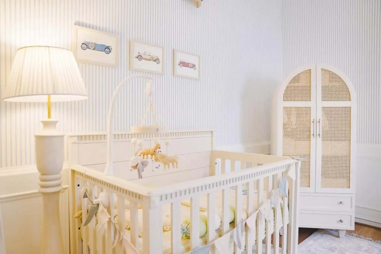 The nursery features a warm crib with toys hanging over it for little one to play. The room also includes frames on cars drawn.