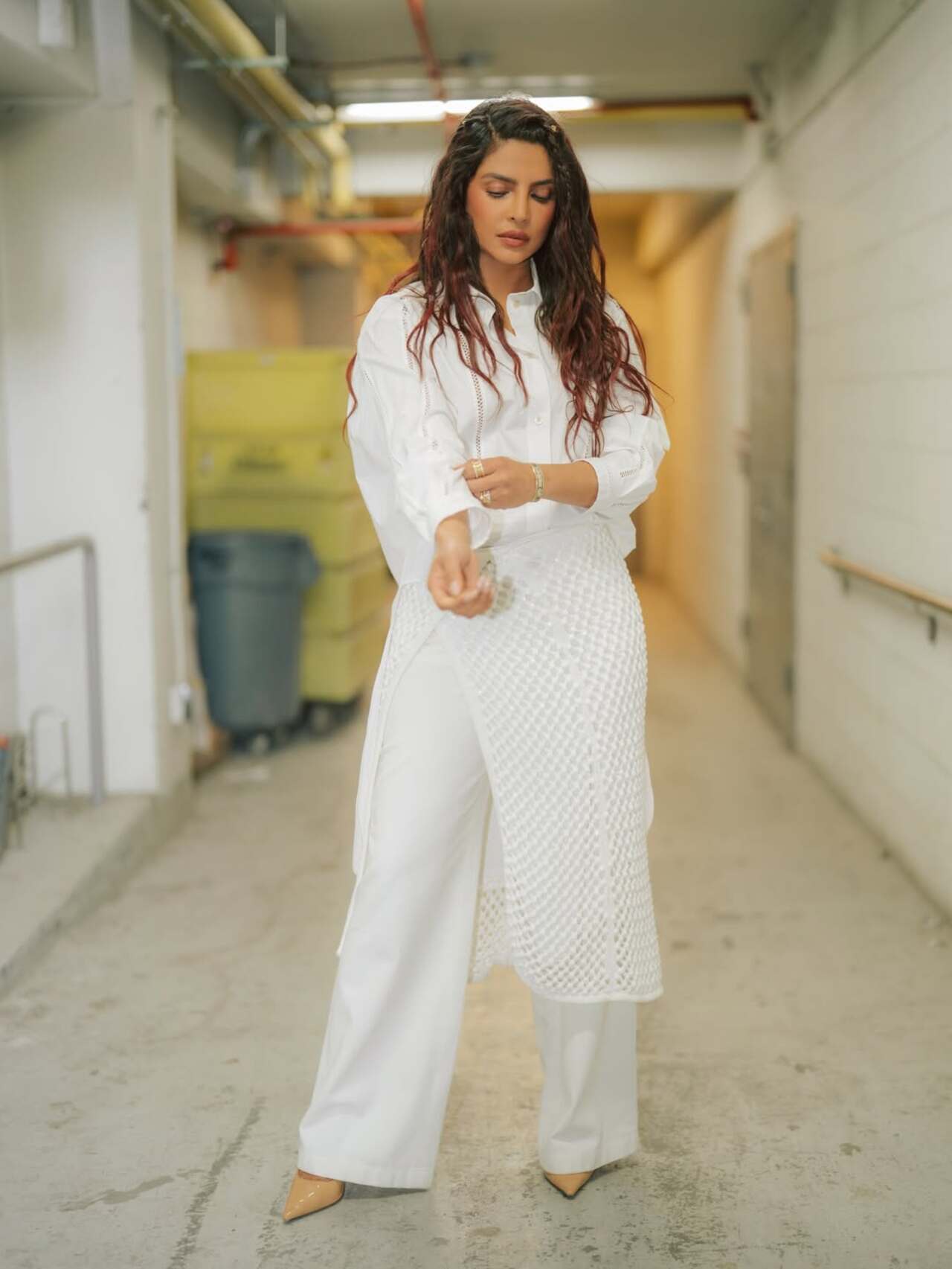 She opted for a crisp white button-down shirt with rolled-up sleeves. The look was elevated with wide-legged white trousers layered with a textured wrap-style skirt detail.