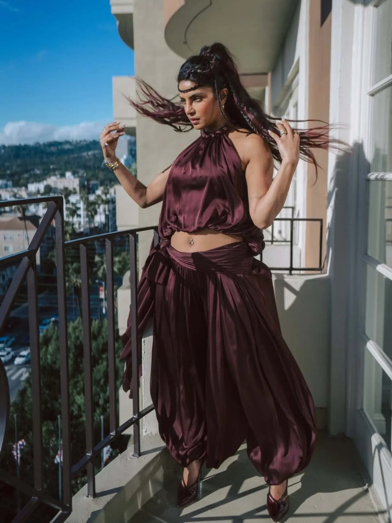 Priyanka Chopra Jonas stuns in a deep burgundy halter-neck outfit featuring a silky draped top and dramatic flowy pants with dewy makeup.