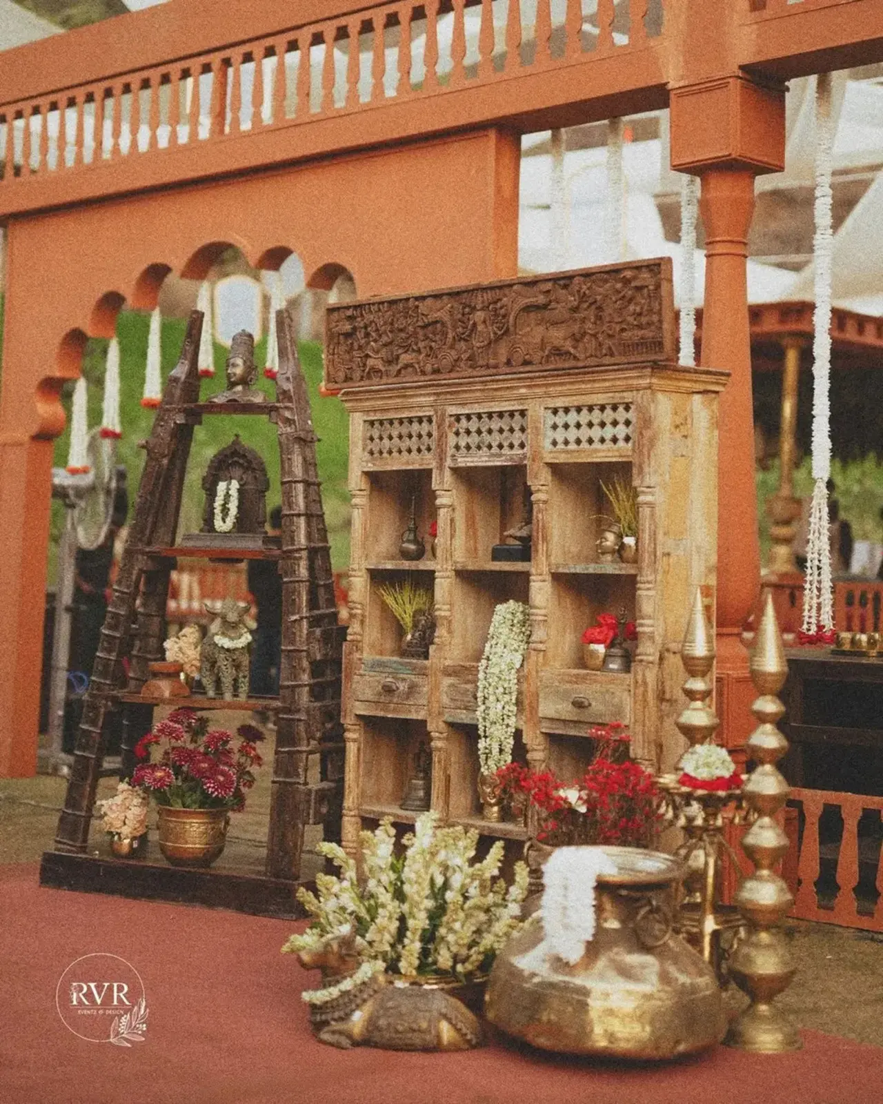 Brass urli bowls, large vintage vases and engraved metal pots are filled with red roses, maroon chrysanthemums and white blooms, adding texture and depth