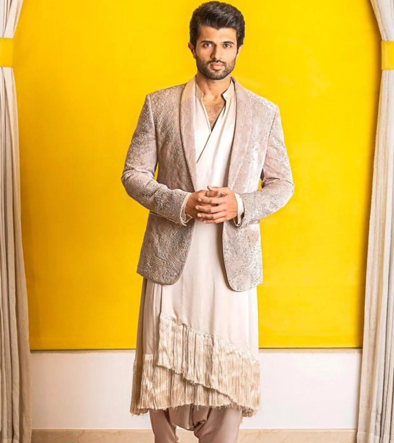 This is Deverakonda at his most experimental. The outfit features an asymmetrical, layered kurta/dhoti pant with a distinctive fringe detail at the hem, creating an artistic, deconstructed drape.