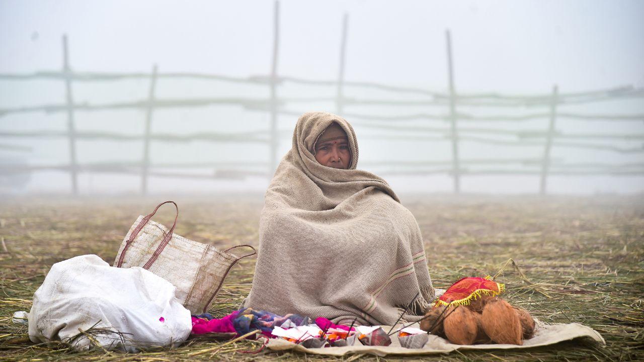 Shrouded in mist, a vendor wrapped in a blanket sits at the Sangam awaiting customers