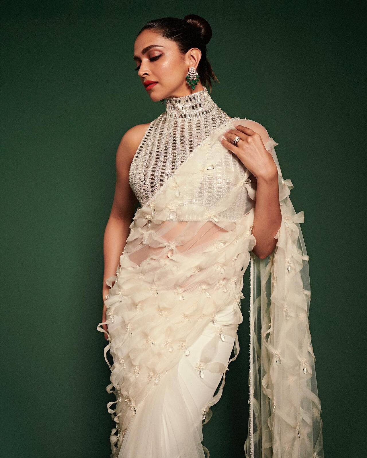 Deepika looked ethereal in a white sheer saree featuring delicate feathered textures. She paired it with a matching blouse adorned with silver mirror work and styled her hair in a neat bun, creating a graceful and festive-ready look perfect.