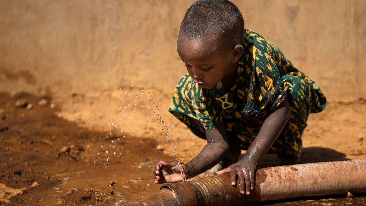 A young girl drinks from a leaking hose at a relief water point in Hawara, illustrating the risks of relying on unsafe water during severe scarcity 