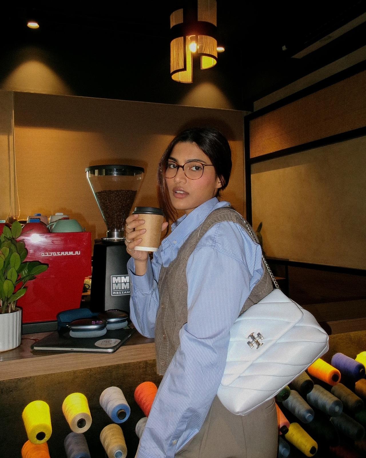 Alizeh opts for a cosy, cafe-chic look, layering a knitted sweater vest over a crisp blue striped shirt. The outfit blends comfort with effortless, winter-ready style.