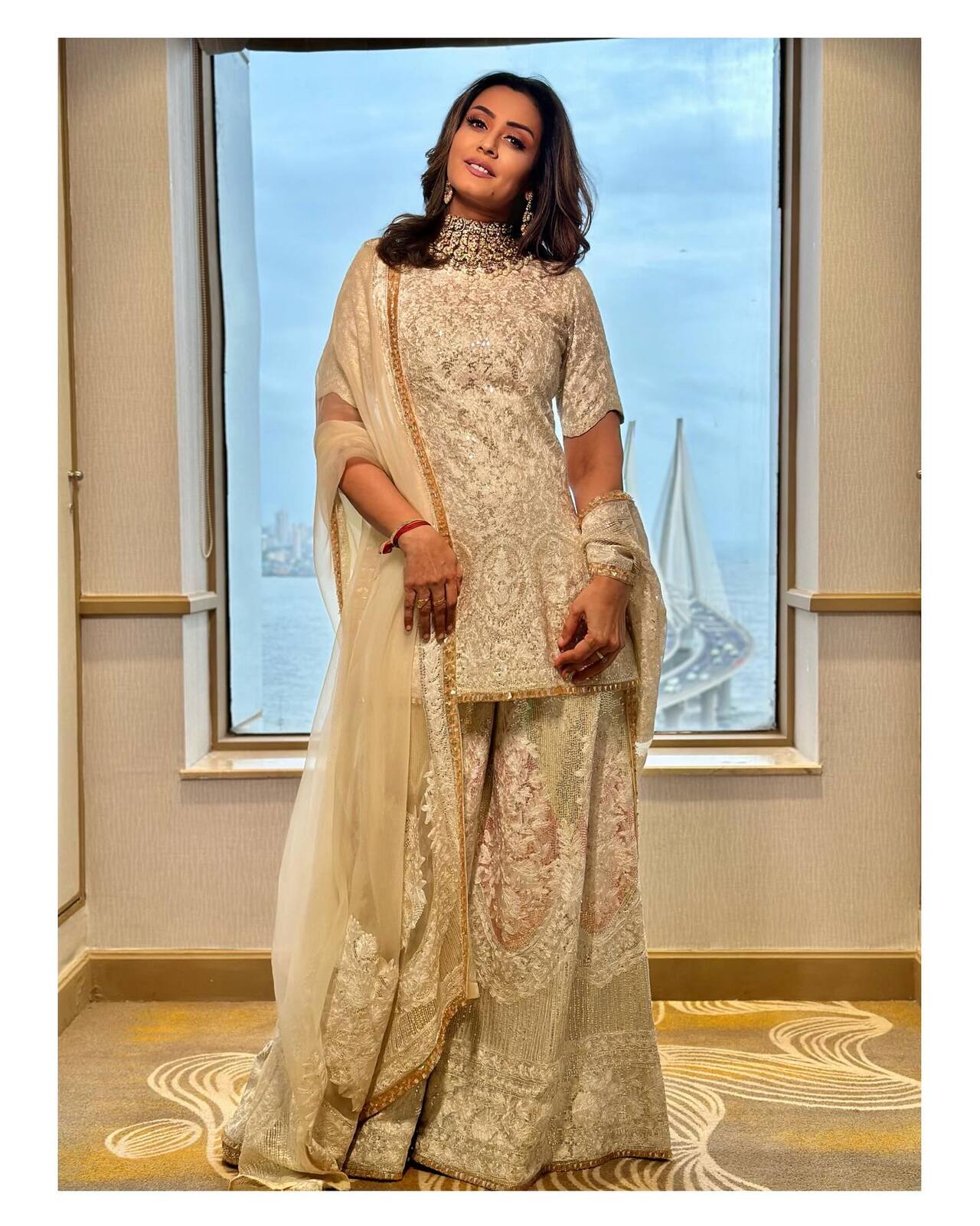 Namrata looks regal in this ivory-hued ensemble featuring a sharara set in a structured silhouette. The delicate, muted gold embroidery and intricate work add a royal and rich feel, while the choker necklace adds to its richness.