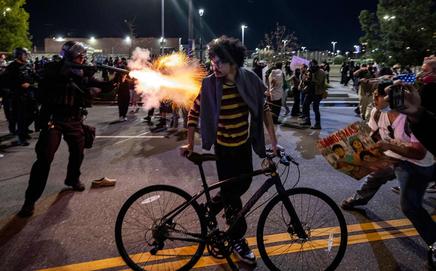 An LAPD officer fires a non-lethal munition while facing protesters during a 