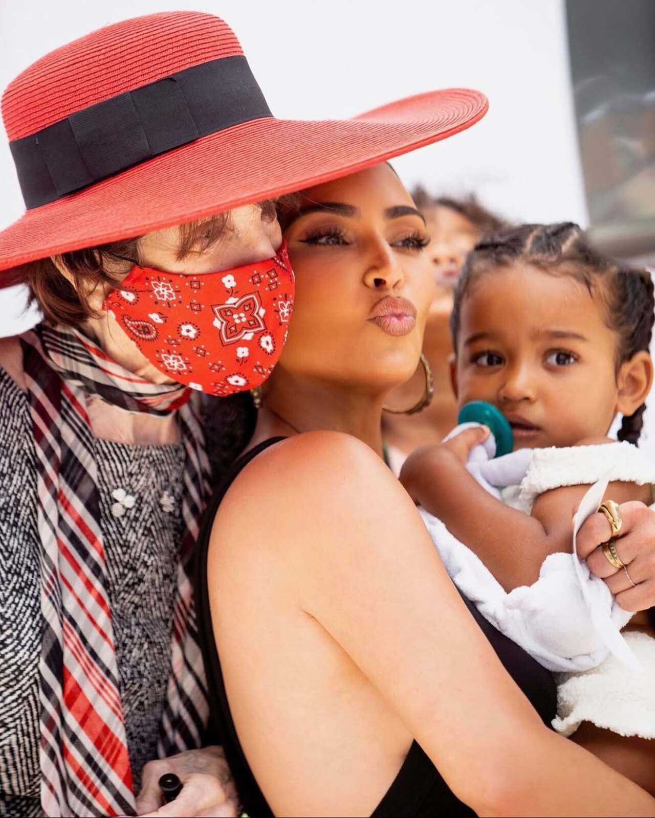 In another candid, MJ hugs Kim from behind while Kim holds a toddler. The image captures a tender three-generation family moment