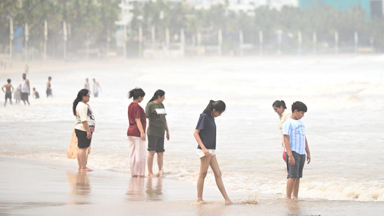 With sea conditions easing, families and visitors spend time by the water as waves lap against the shore at Juhu Beach
