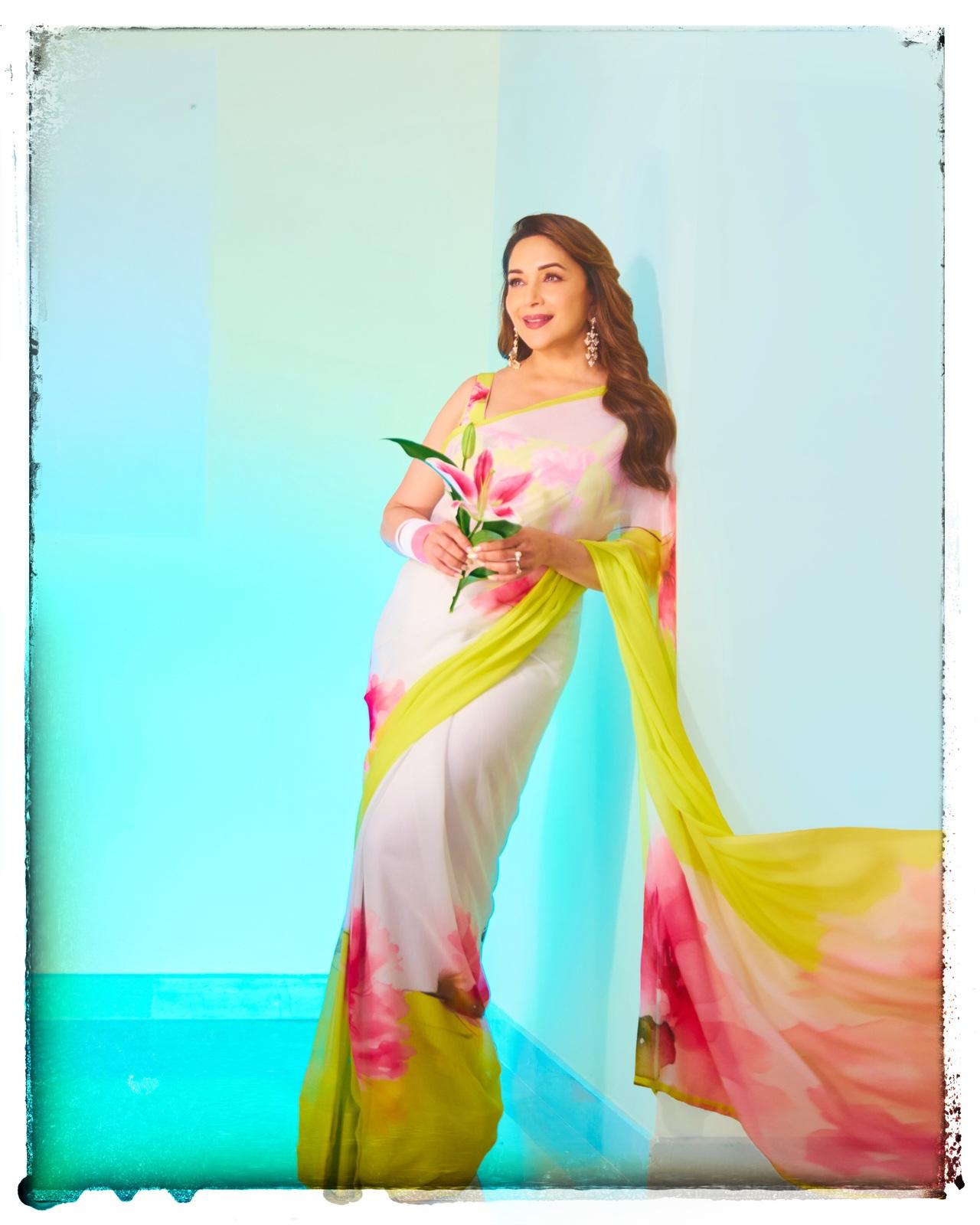 Madhuri Dixit looks breathtakingly radiant in a lightweight chiffon saree featuring a beautiful blend of white, vibrant pink floral patterns, and a refreshing lime-green border.
