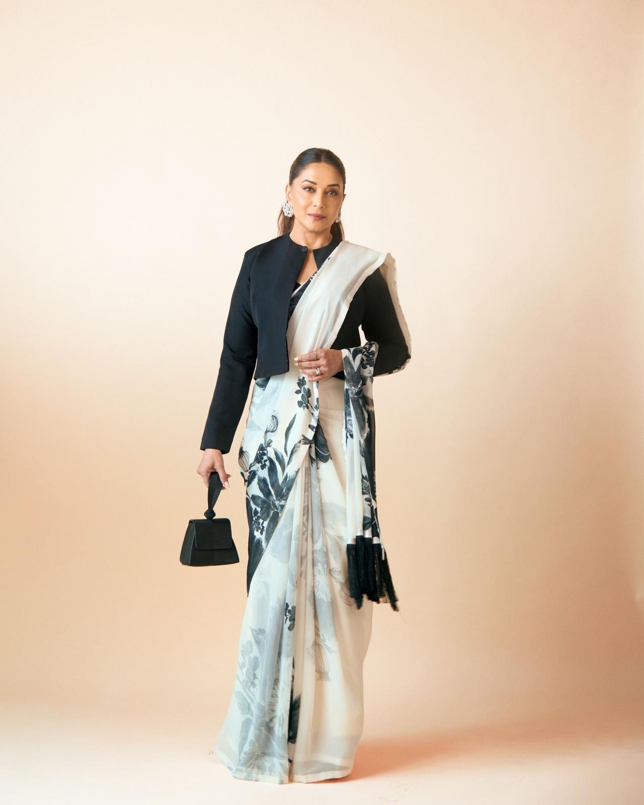 Madhuri Dixit exudes contemporary sophistication in a striking monochromatic look, pairing an elegant white saree featuring bold black floral prints with a structured, full-sleeved black jacket.
