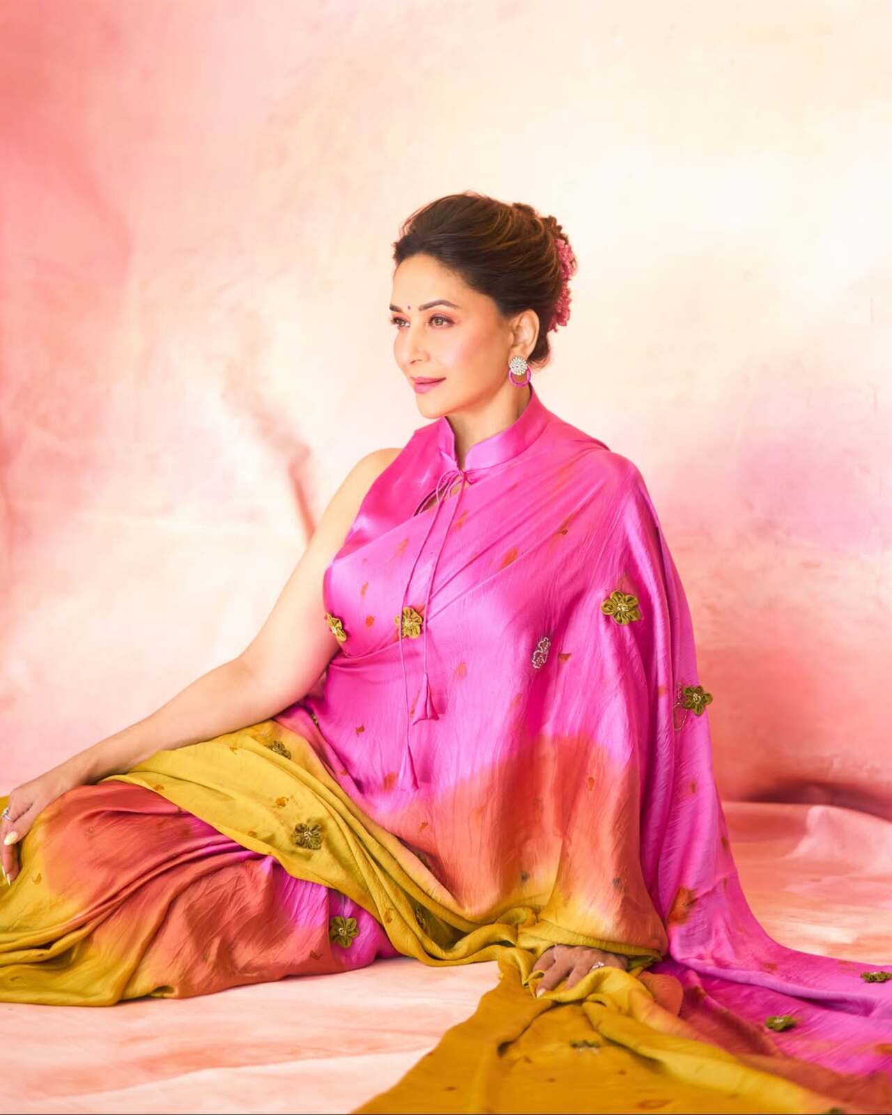 She pairs the elegant drape with a matching sleeveless, high-collared pink blouse, statement stud earrings, and an elegant updo adorned with matching pink flowers.
