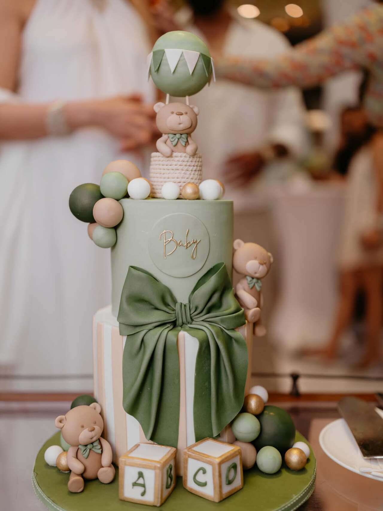 A stunning multi-tier cake became one of the highlights of the celebration. Decorated in soft green and beige hues, the cake featured teddy bear figurines, pastel balloons, alphabet blocks and a large bow.