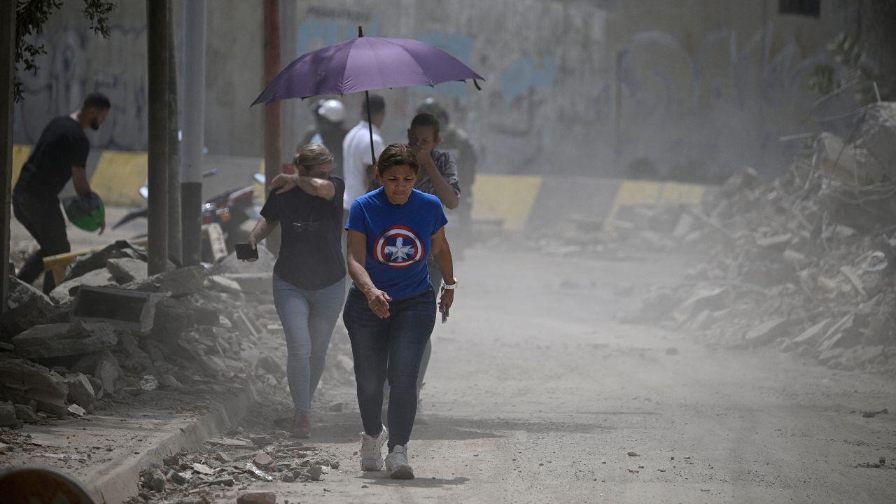 Residents walk along a debris-strewn street as dust hangs in the air following an earthquake in Catia La Mar