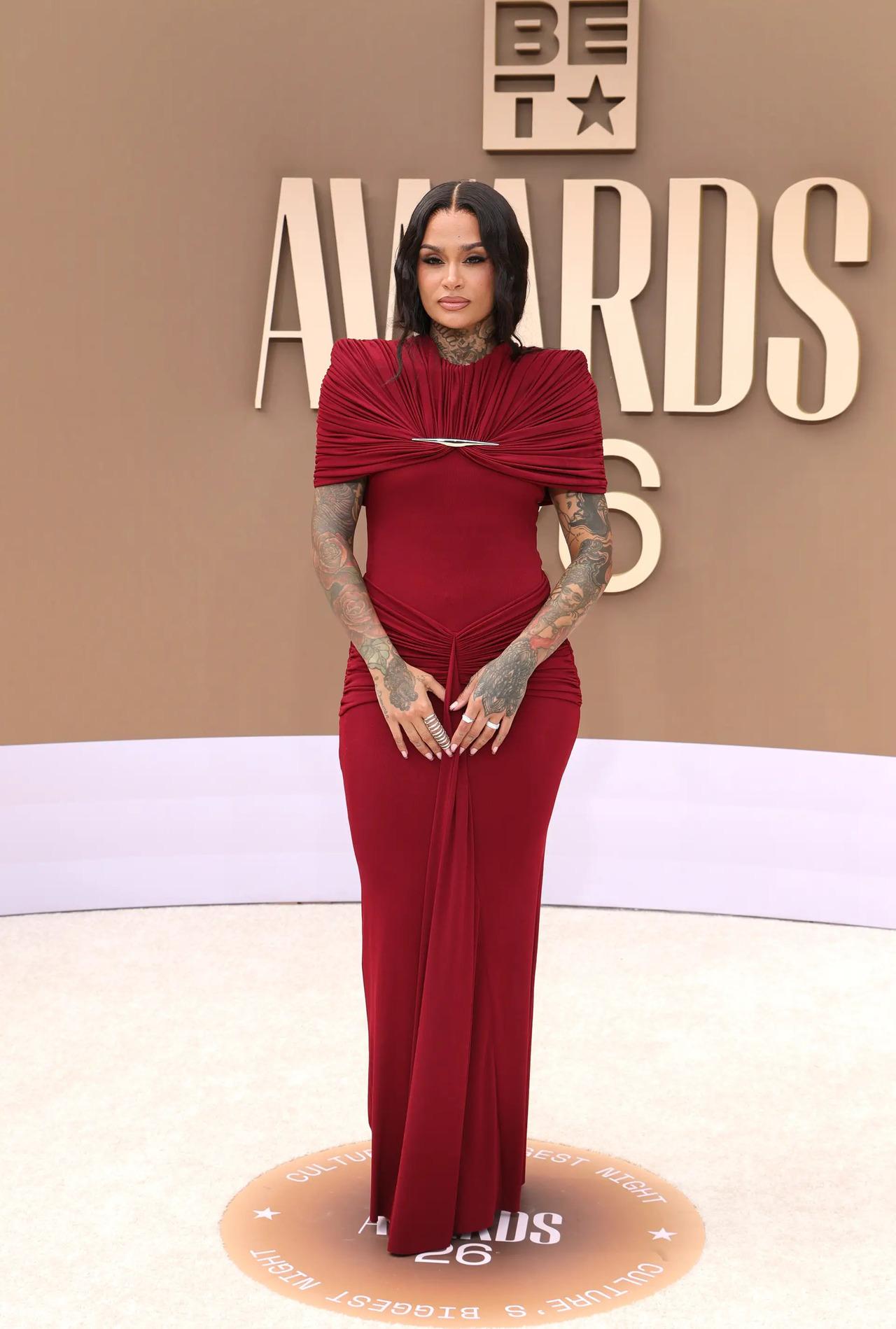 Kehlani made a bold fashion statement in a fitted burgundy gown featuring a dramatic pleated neckline and elegant draping.