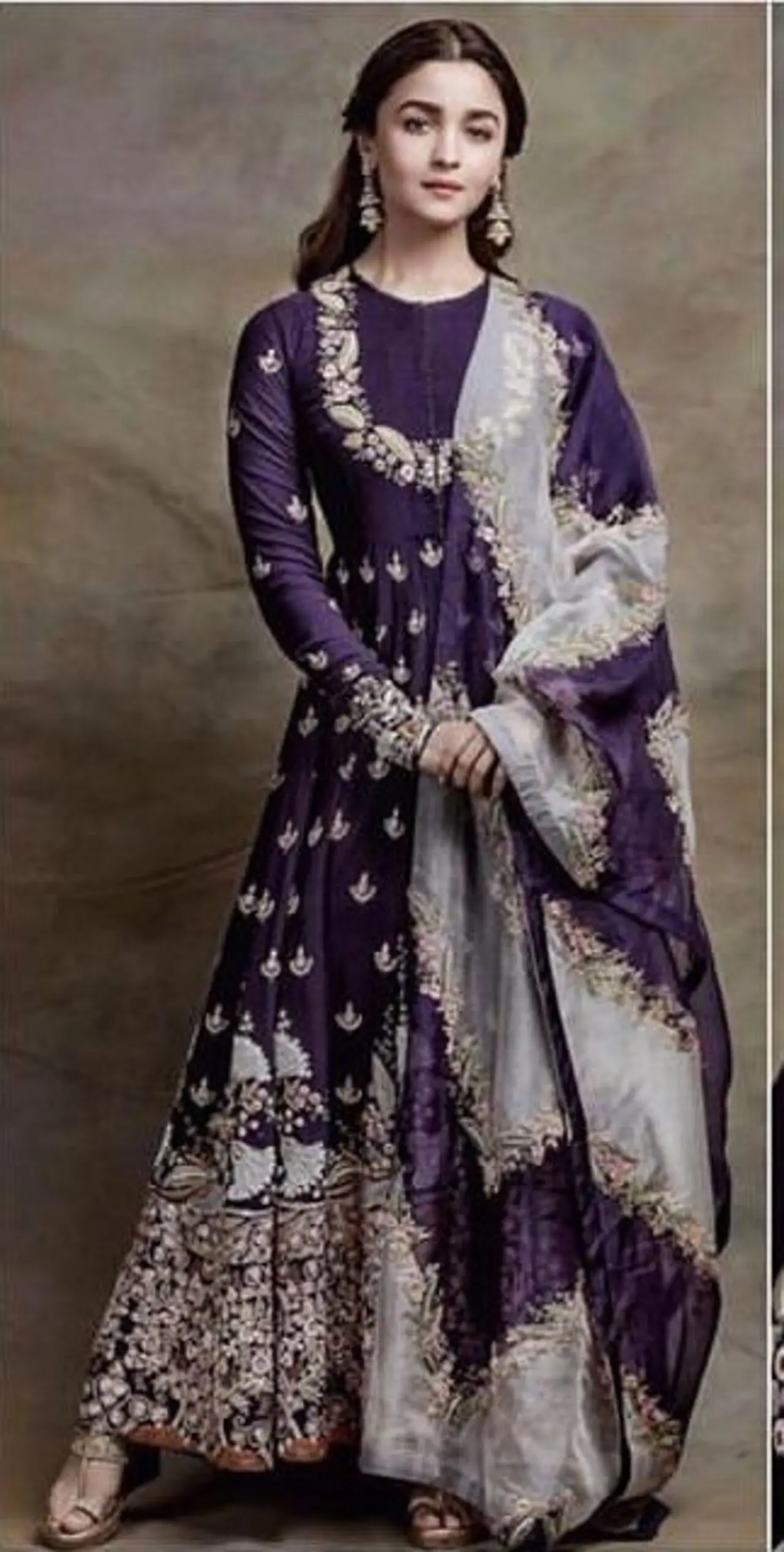 Alia Bhatt stuns in this purple floor-length anarkali suit featuring intricate white and gold-toned embroidery and embellishments. Her earrings and half-tied hair perfectly complement the outfit.