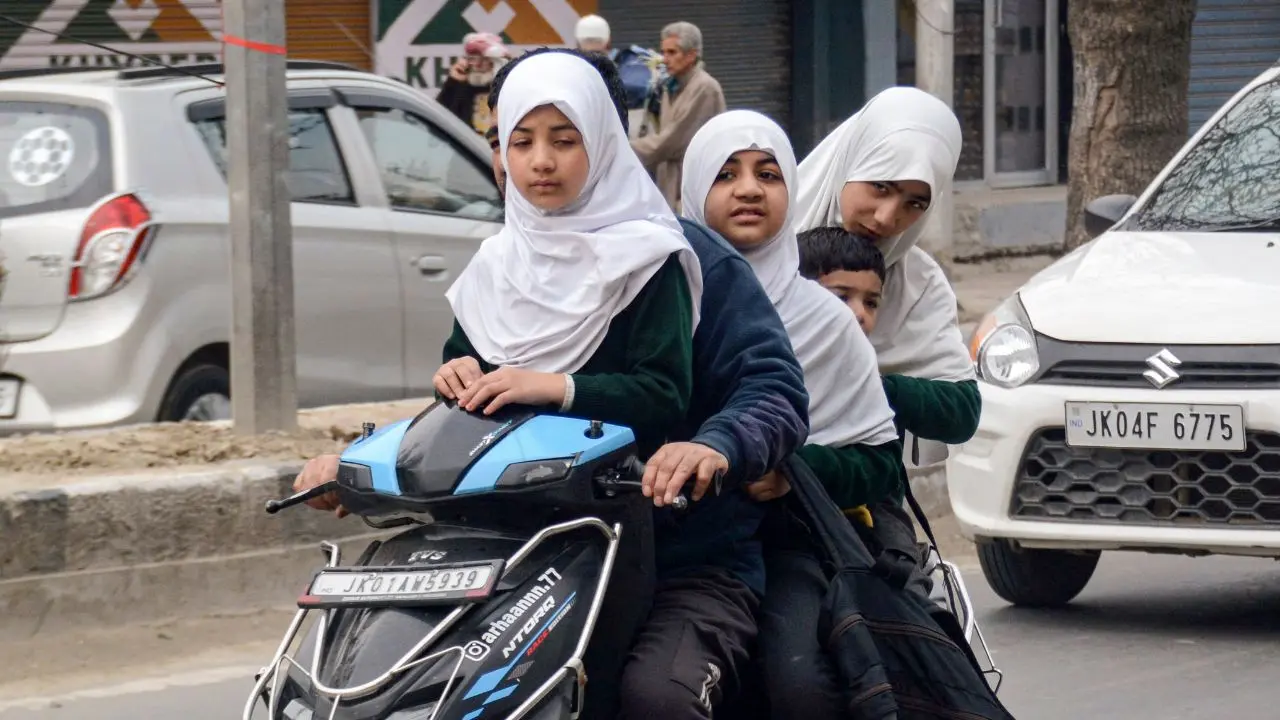 <p>A man rides a two-wheeler with his four children heading to school, marking the first day back for students after protests delayed reopening</p>