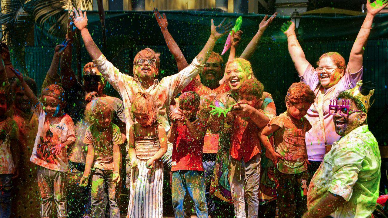 People and children smeared in colours pose for photographs during celebrations of the 'Holi' festival, in Mumbai