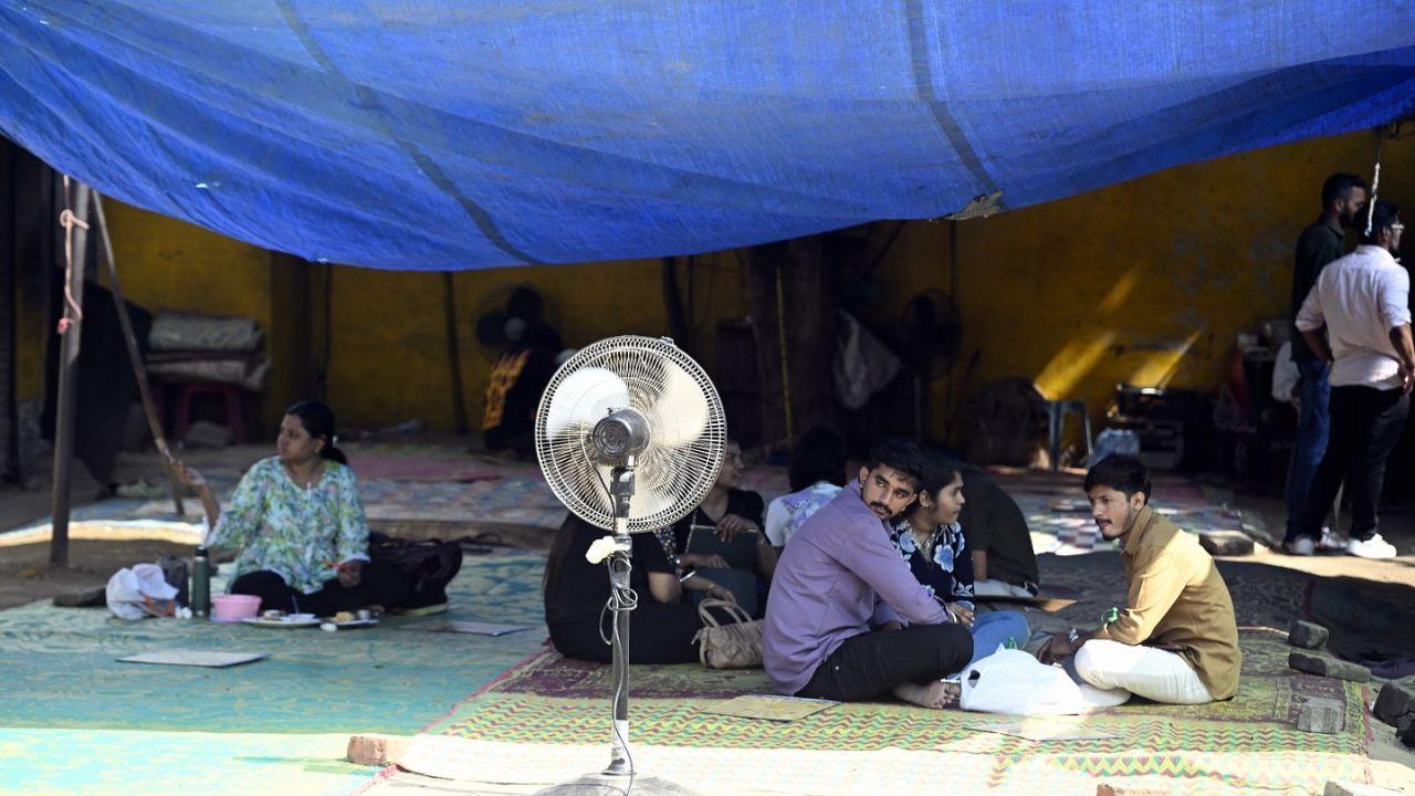 People take shelter near a fan at a makeshift spot to beat the afternoon heat at Mumbai’s Chowpatty on Wednesday.