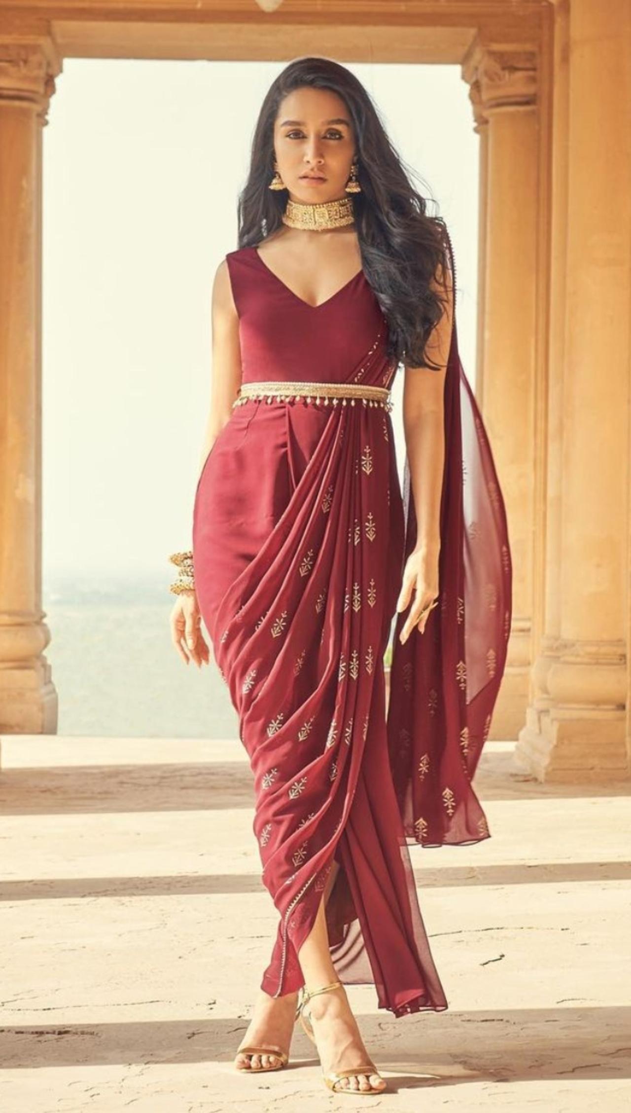 Shraddha wears a modern, maroon pre-draped dhoti-style saree with a waist belt, showcasing a blend of traditional and contemporary fashion. 
