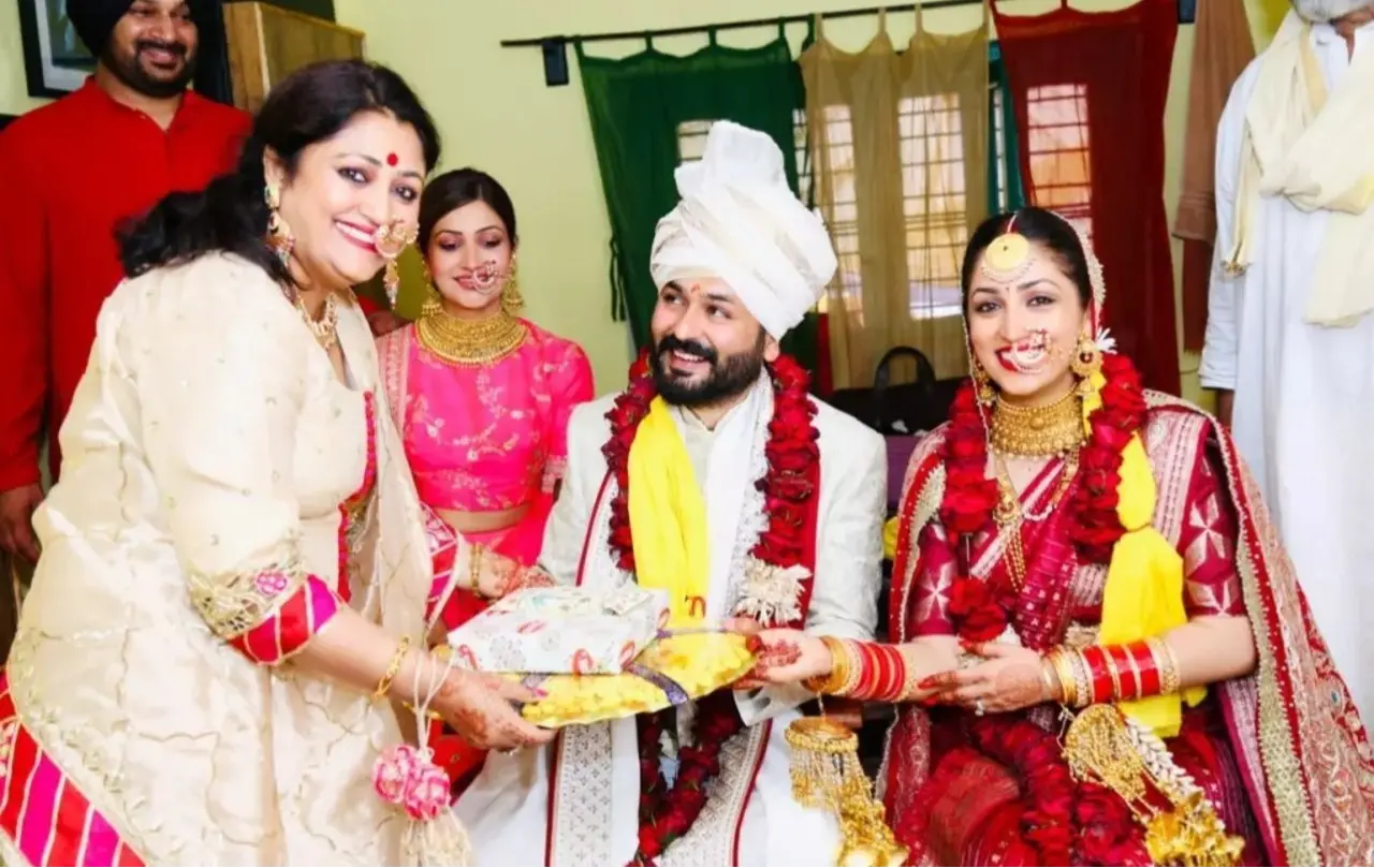 Yami's mother performs the wedding rituals by giving them gifts as they newly married couple sit and pose for a picture.