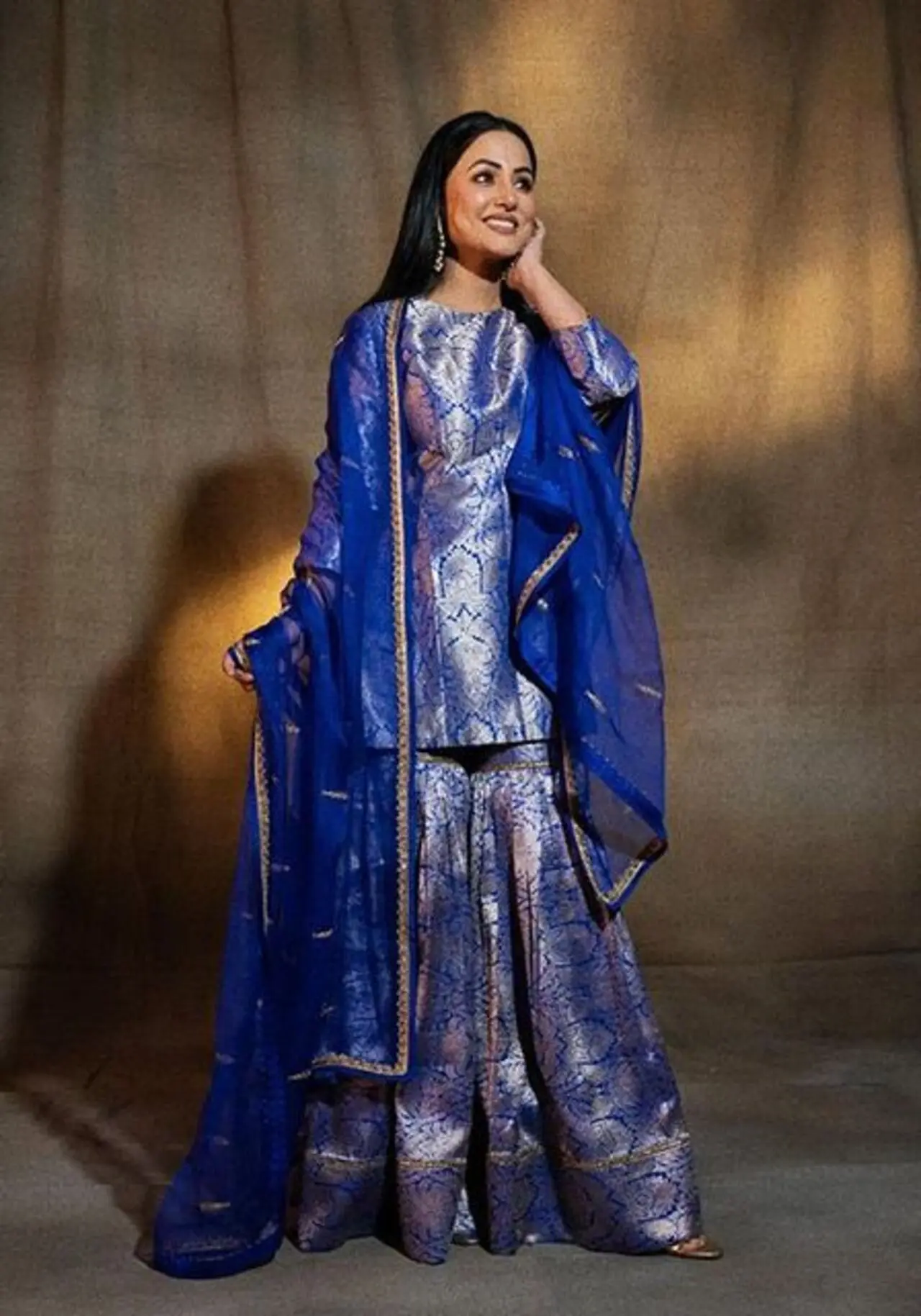 Hina Khan sets the mood for Eid in this blue Banarasi silk sharara set with gold and silver brocade work. The set is paired with a matching sheer dupatta with gold borders.