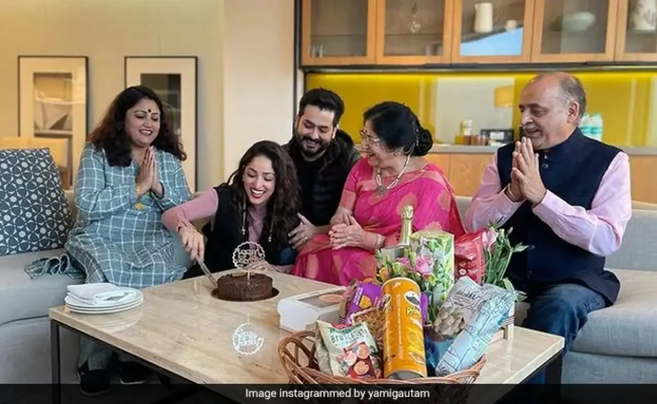 Aditya, along with his parents and Yami's mother, celebrate the actress's birthday, as she excitedly cuts the cake and all of them clap.