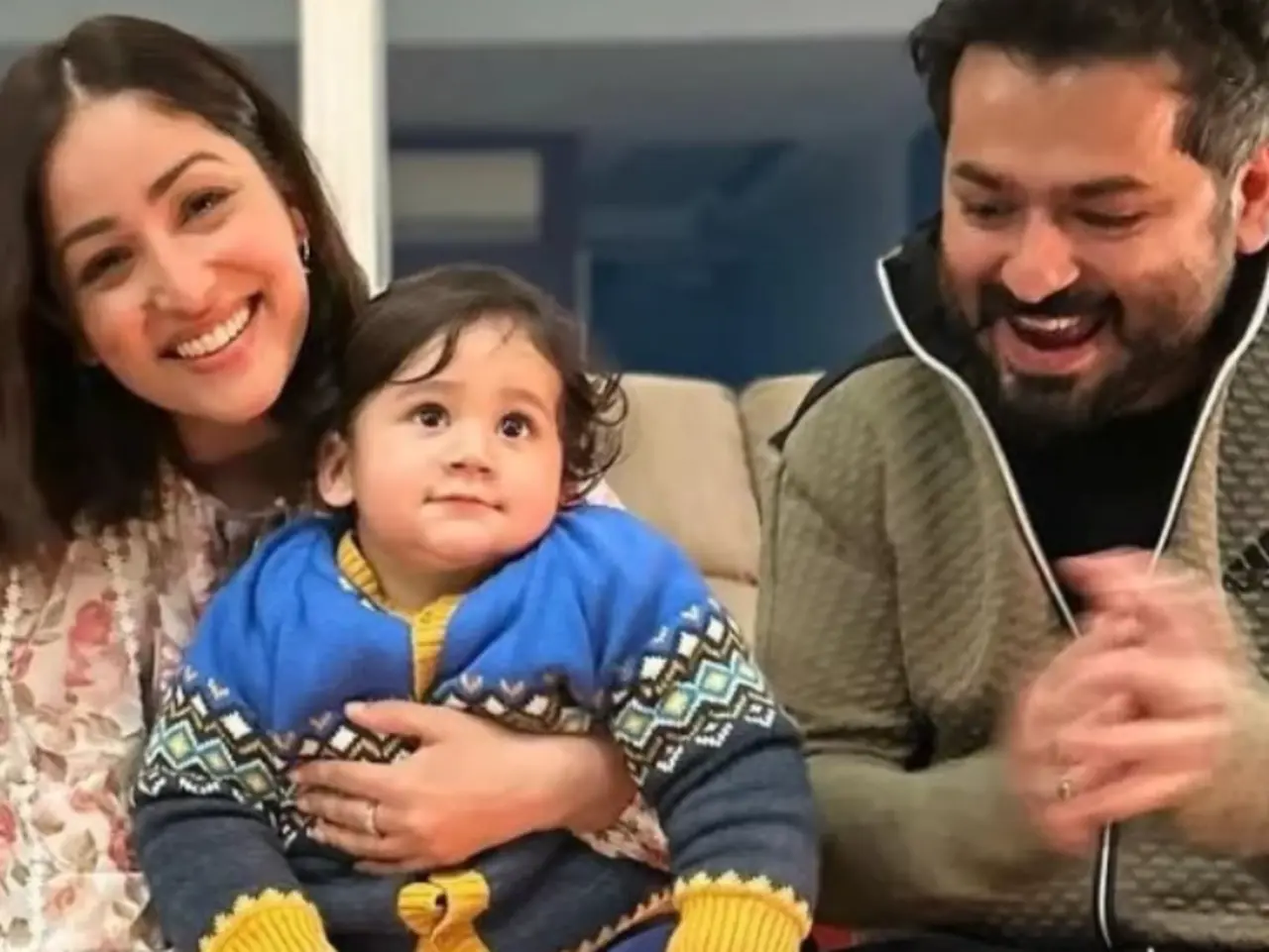 An adorable family photo has Aditya excitedly cheering for his son, Vedavid, as he sits on mother Yami's lap, while she smiles for the camera.