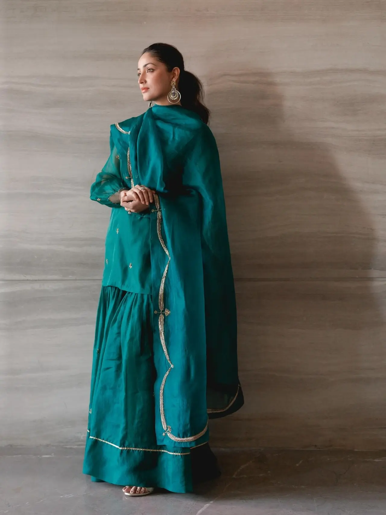 Yami Gautam shows how to keep it laid back and comfy in this green short kurta paired with sharara pants and a dupatta. It is a plain outfit accentuated by delicate gold trim or embroidery along the edges of the kurta, dupatta, and the hem of the sharara pants. 
