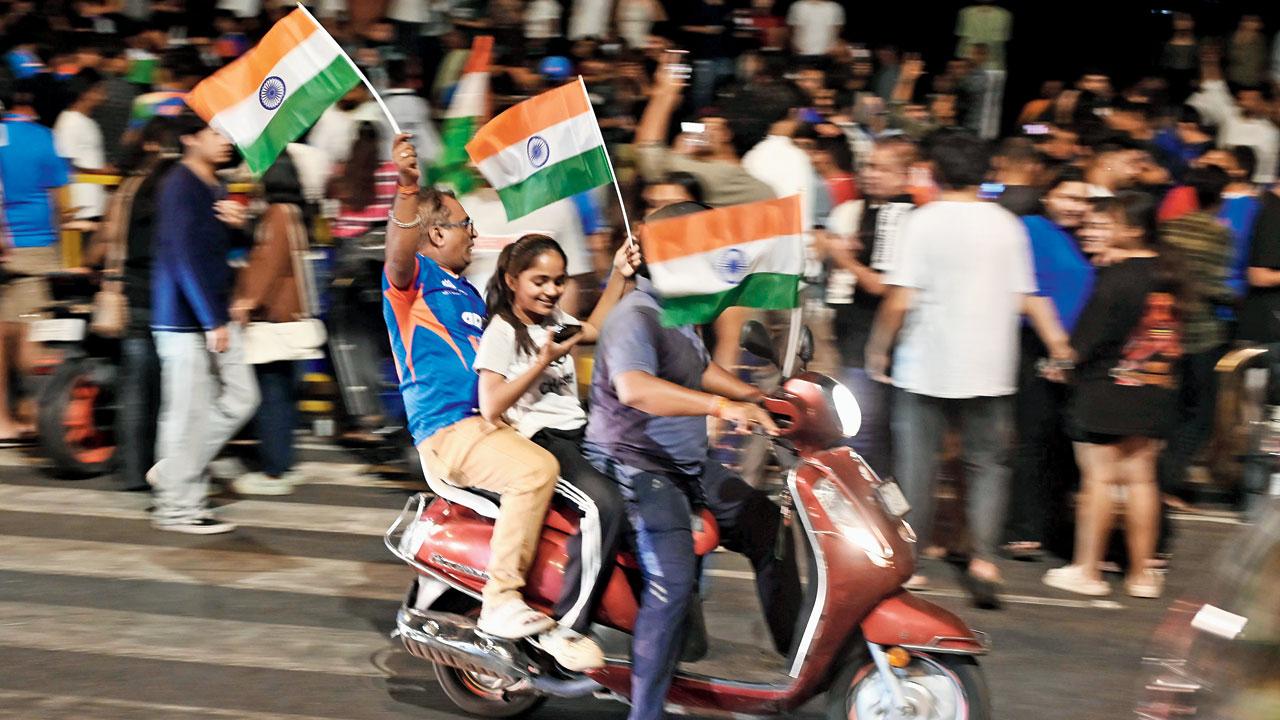 Three Indian cricket team fans wave the Indian flag as they make way through the traffic