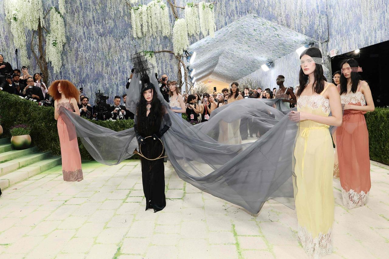 Madonna delivered a strikingly theatrical look at the Met Gala, leaning into gothic drama and avant-garde storytelling. Dressed in an all-black ensemble, she wore a flowing, sheer veil that extended dramatically, carried by models to create a haunting, almost ritualistic visual.&nbsp;
