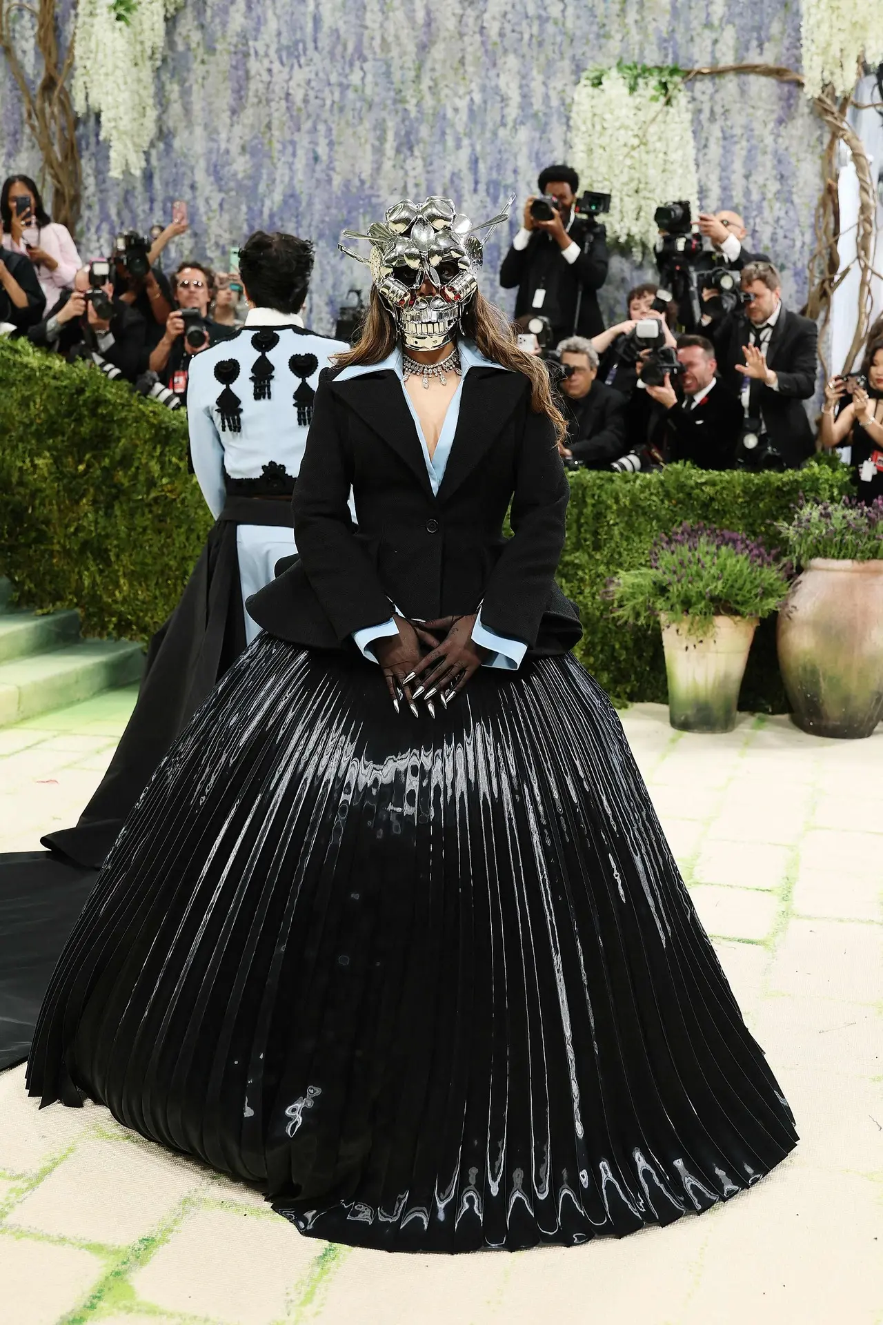 For her appearance, Ananya Birla wore a custom creation by Robert Wun, paired with a sculptural mask designed by artist Subodh Gupta. The outfit featured a structured black jacket with a dramatic peplum and a voluminous pleated skirt, giving it a strong, sculpted silhouette. The most eye-catching element of the look was the metallic face mask made using stainless steel.