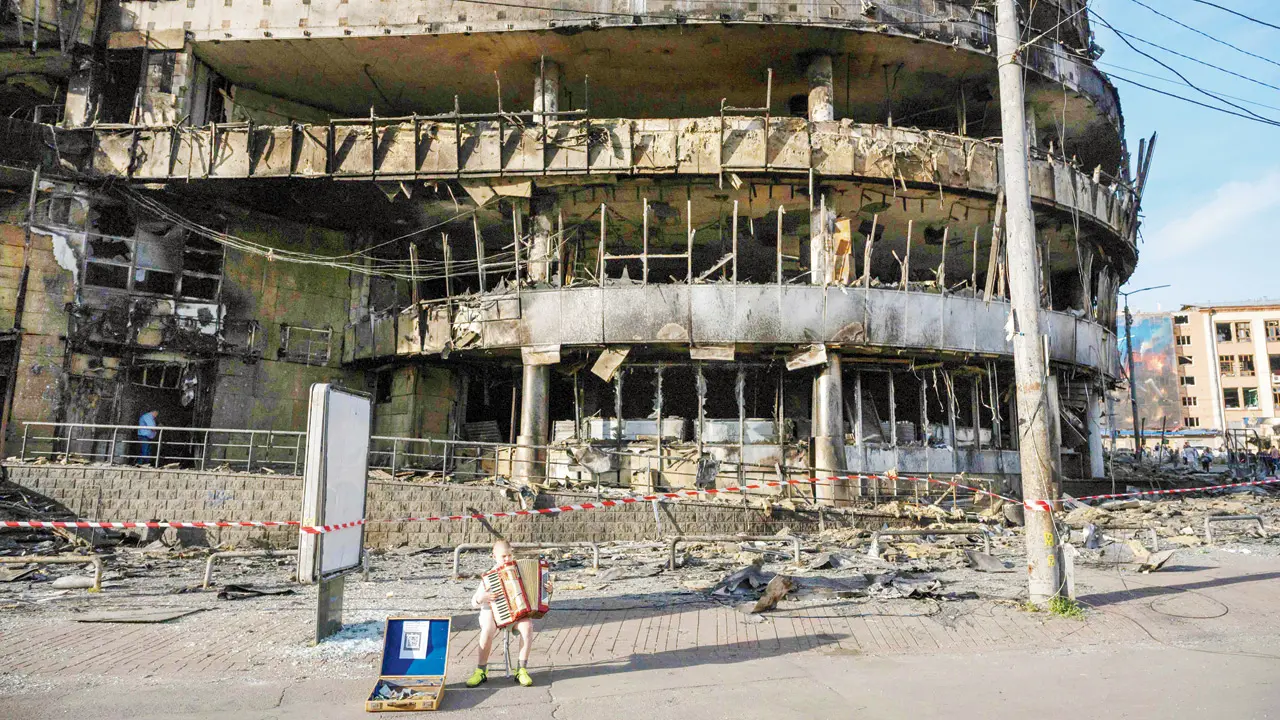 A boy plays the accordion in front of a shopping centre damaged by Russian strikes in Kyiv, on Monday. PIC/AFP