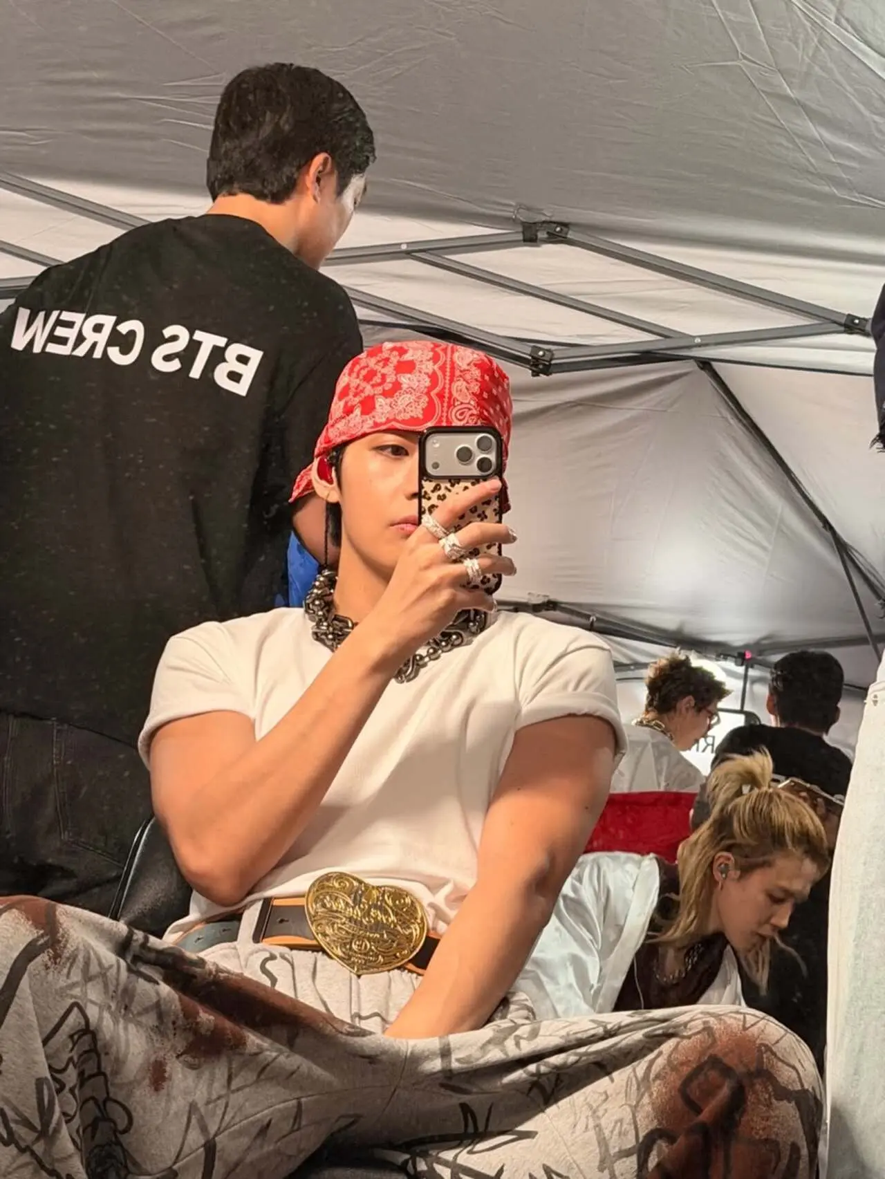 Seated under a tented setup, with crew members in the background, the candid shot captures a behind-the-scenes moment from his tour prep.