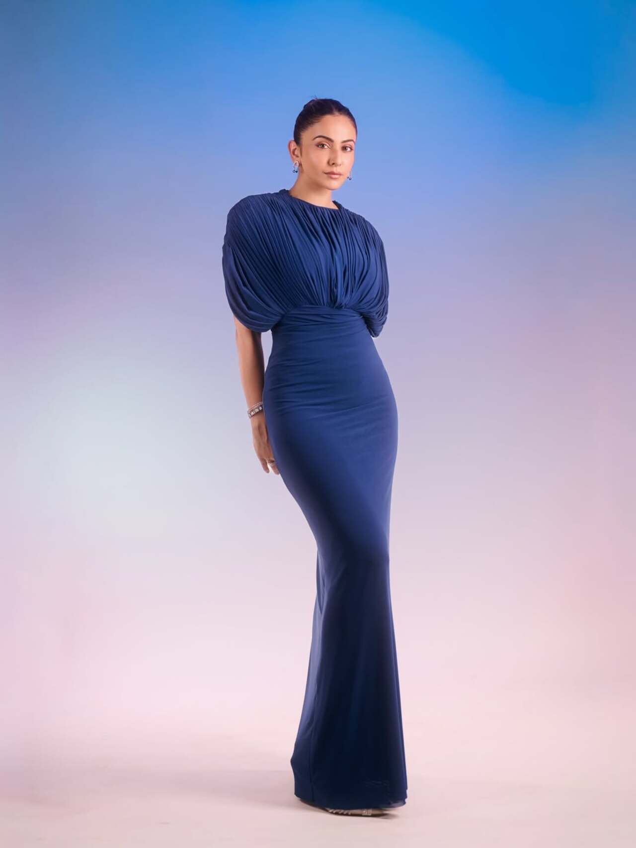 Rakul Preet Singh looks stunning in a deep blue floor-length gown. The dress features a unique pleated design on the top with puffed sleeves and a fitted skirt. Rakul Preet Singh looks stunning in a deep blue floor-length gown. The dress features a unique pleated design on the top with puffed sleeves and a fitted skirt.