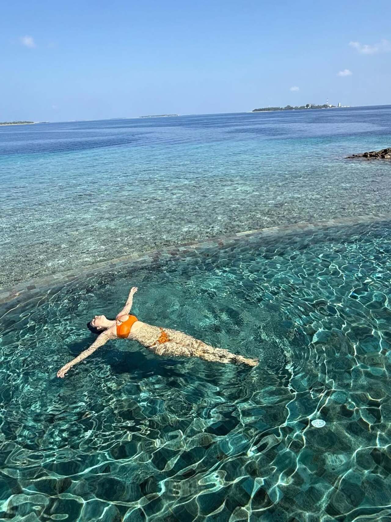 Kiara Advani embraces pure serenity as she floats effortlessly in a crystal-clear infinity pool, dressed in a vibrant orange bikini.