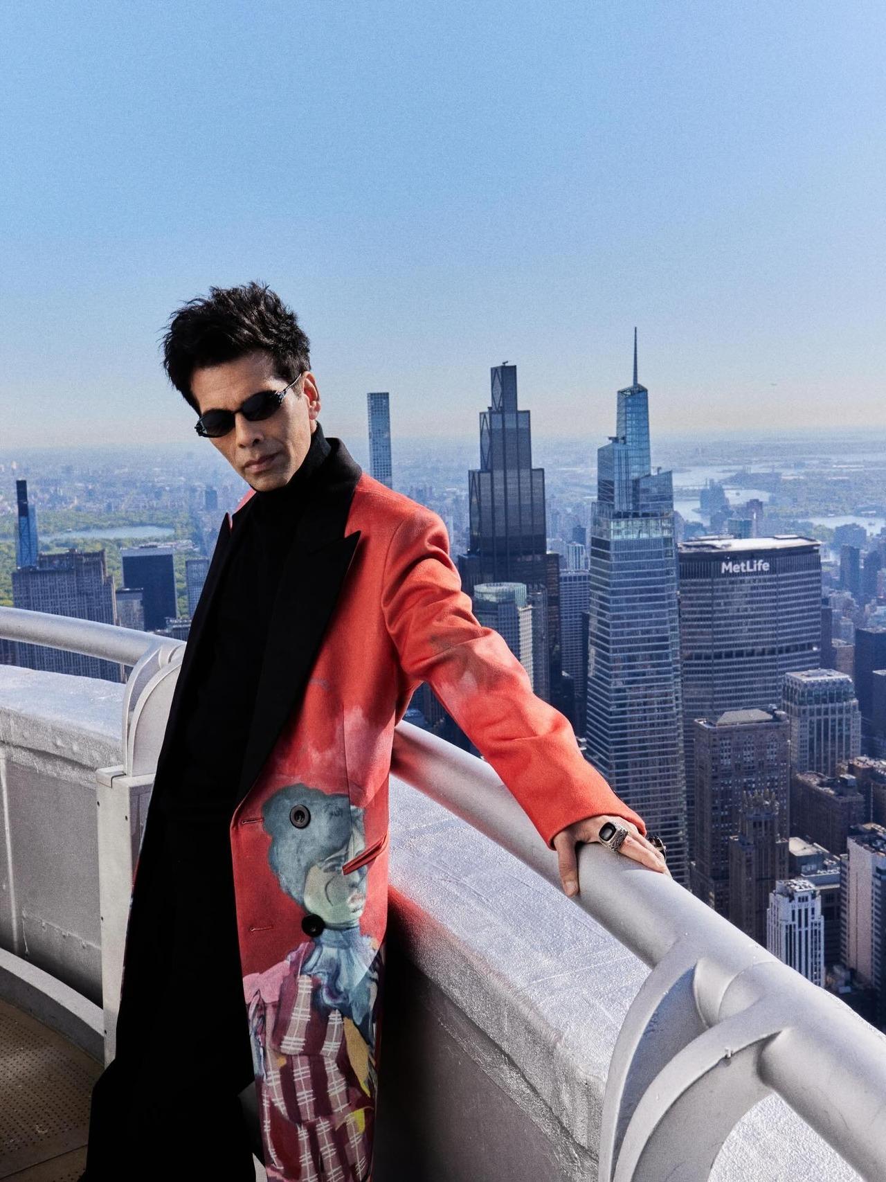 Posing against the skyline of New York, Karan Johar exudes style and class in a striking red KidSuper Watercolour Girl Coat, layered over a black turtleneck t-shirt.