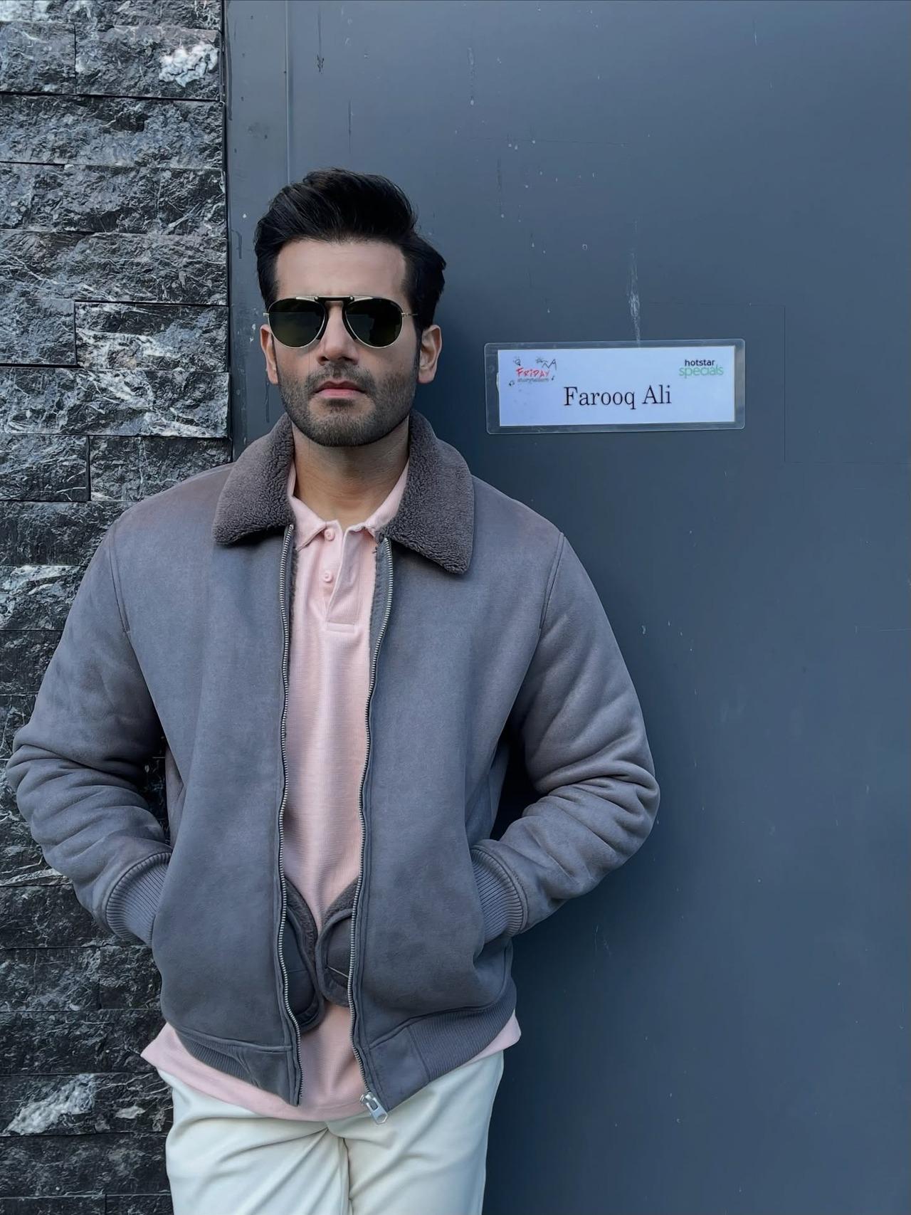 Karan elevates a simple grey faux suede bomber jacket, pairing it with a pink polo t-shirt and white pants. Karan elevates a simple grey faux suede bomber jacket, pairing it with a pink polo t-shirt and white pants.
